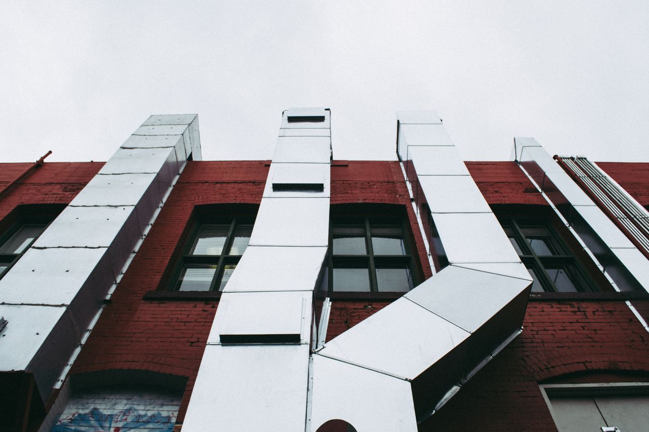 about-01 Low angle view of a modern industrial facade with prominent metal ducts on a red brick building.
